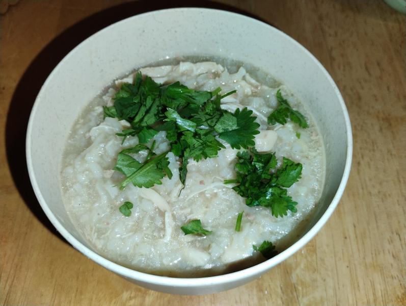 A small bowl holding a stew of rice and shredded chicken, garnished with cilantro. The broth has a lovely shimmer and the rice is cooked until nearly falling apart.